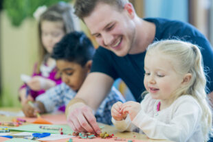 Young children being helped to colour with crayons