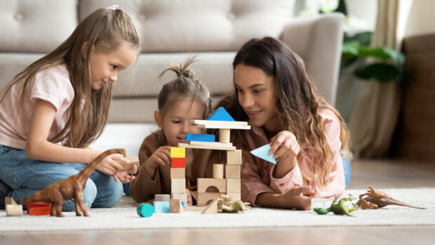 An adult and two children play with wooden blocks and other toys